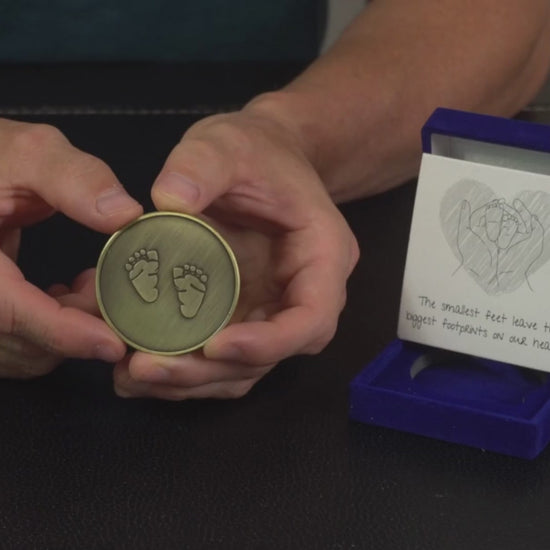 man shows miscarriage memorial coin with baby feet engraved on it. He reviews a miscarriage gift for dad.