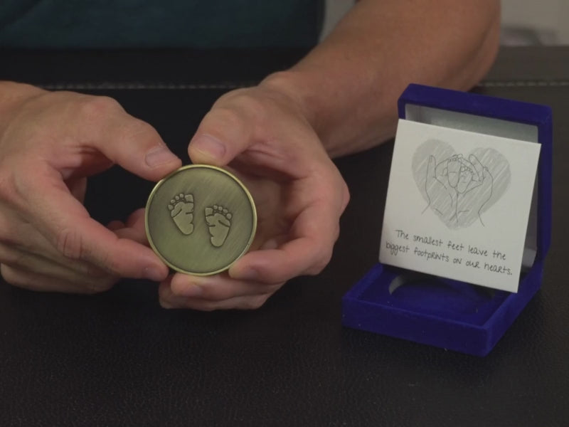 man shows miscarriage memorial coin with baby feet engraved on it. He reviews a miscarriage gift for dad.